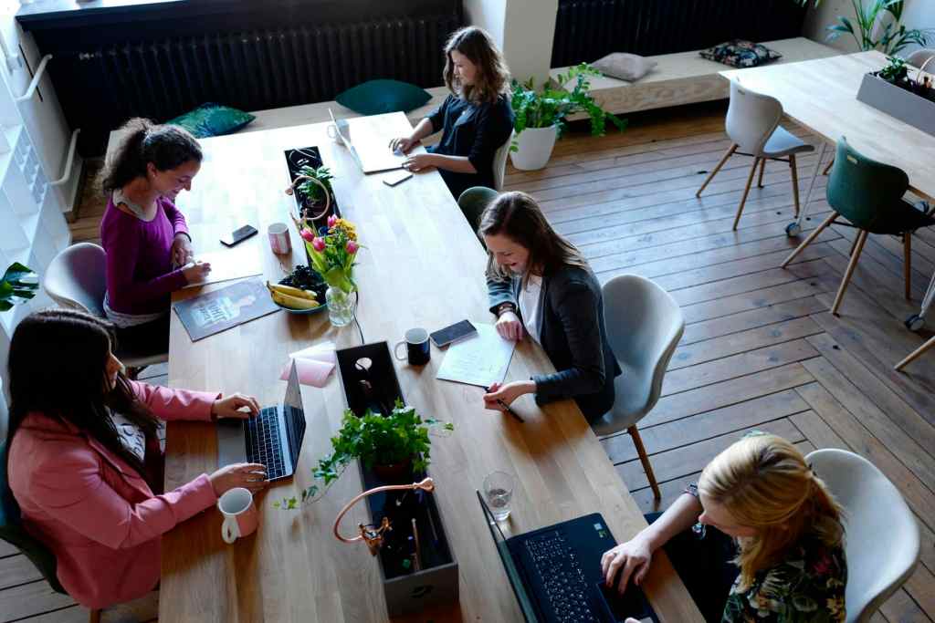 a group of people sitting around a wooden co-working space table